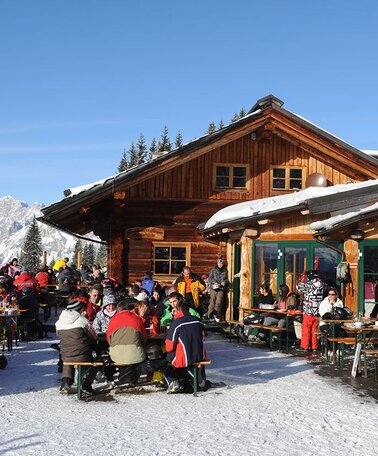 Die Weitmoosalm | © Weitmoosalm Holzhütte im Schnee mit Terrasse voll mit Menschen | © Weitmoosalm